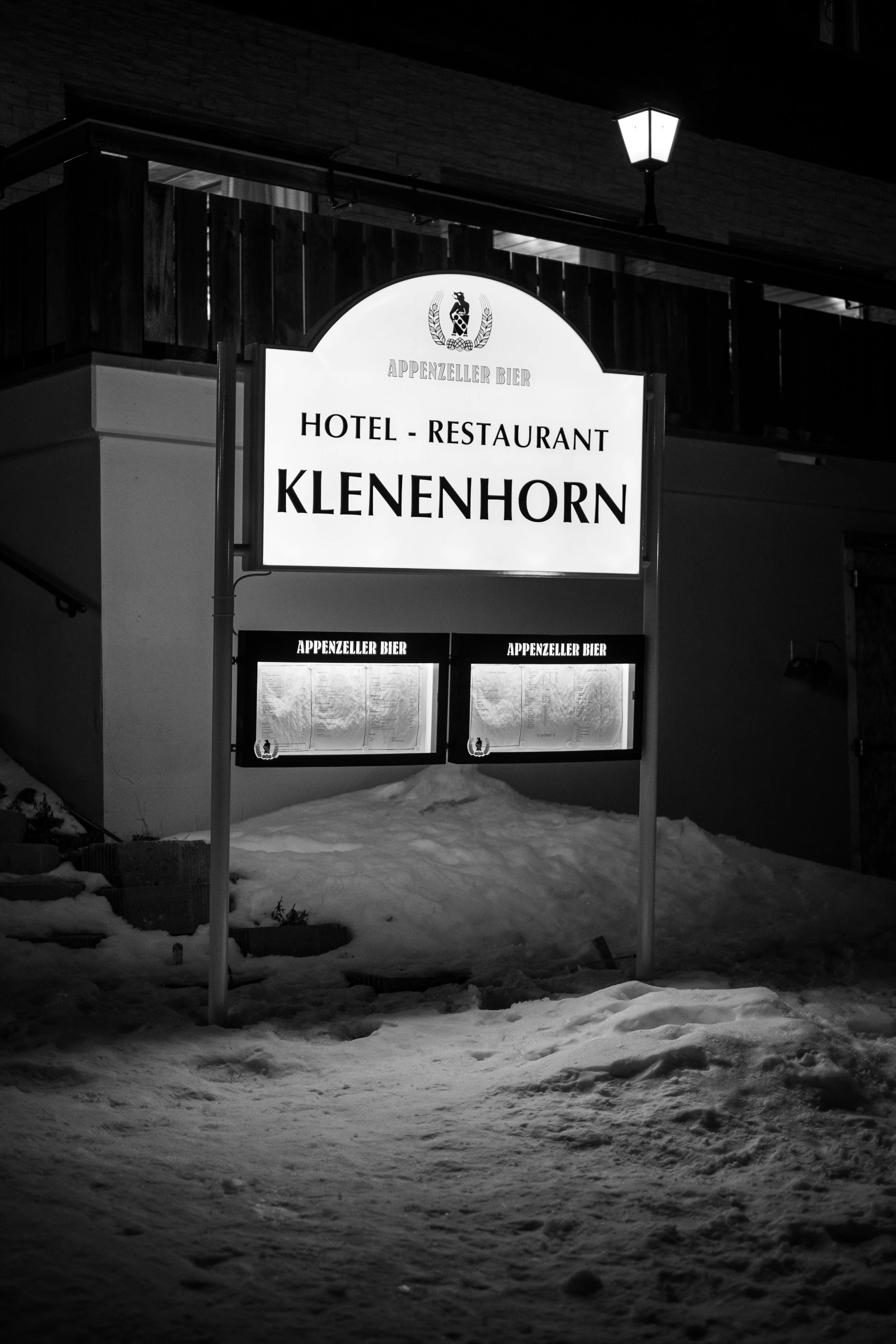 Schriftzug für Hotel und Restaurant Klenenhorn mit dem Logo von Appenzeller Bier vor einem dunklen Gebäude bei Schneem entorno. 