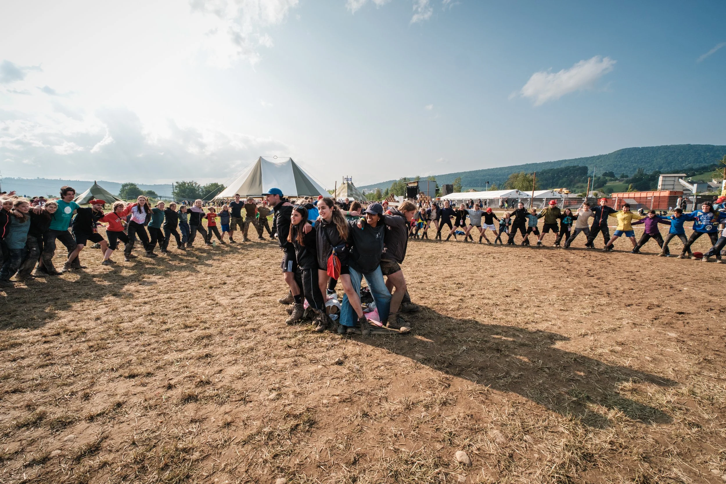 Menschen beim Teambuilding-Spiel, das sich auf einem Feld mit kargem Boden im Freien unter einem blauen Himmel mit wenigen Wolken befindet.