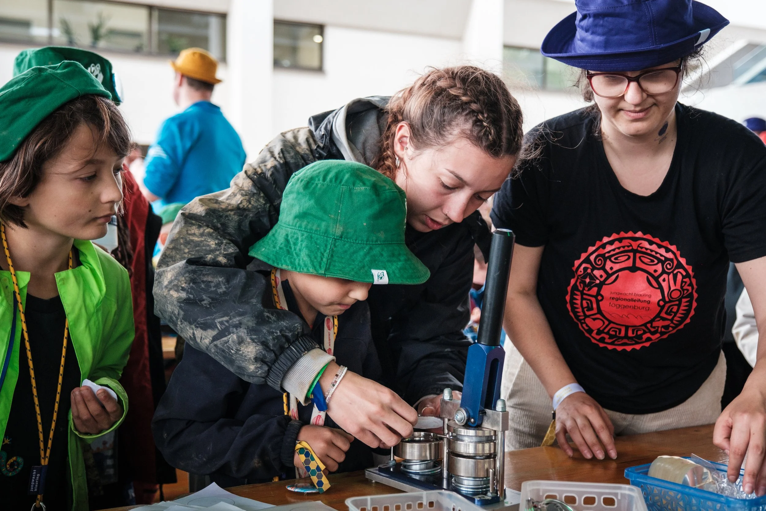 Kinder und Betreuer beim Basteln mit Metall, umgeben von Bastelmaterialien, in einem Innenraum, vermutlich bei einer Aktivität oder einem Workshop.